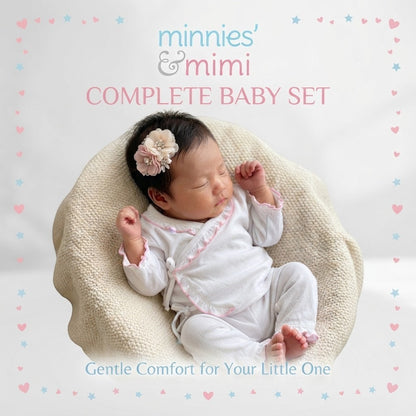 A sleeping newborn baby wearing a white and pink outfit, resting in a beige textured bassinet. The baby has a pink and beige flower hair clip.