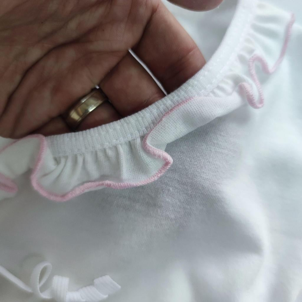 Close-up of a white garment with pink trim held by a hand wearing a gold ring.