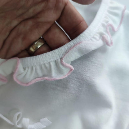 Close-up of a white garment with pink trim held by a hand wearing a gold ring.